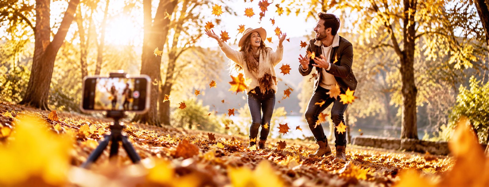 Couple faisant une séance photo en automne avec un téléphone posé sur un trépied au milieu des feuilles dorées